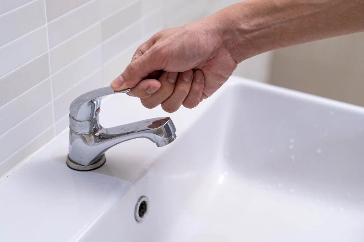 Hand dreht Wasserhahn auf